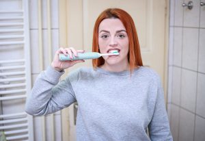 אישה מצחצת שיניים עם מברשת חשמלית